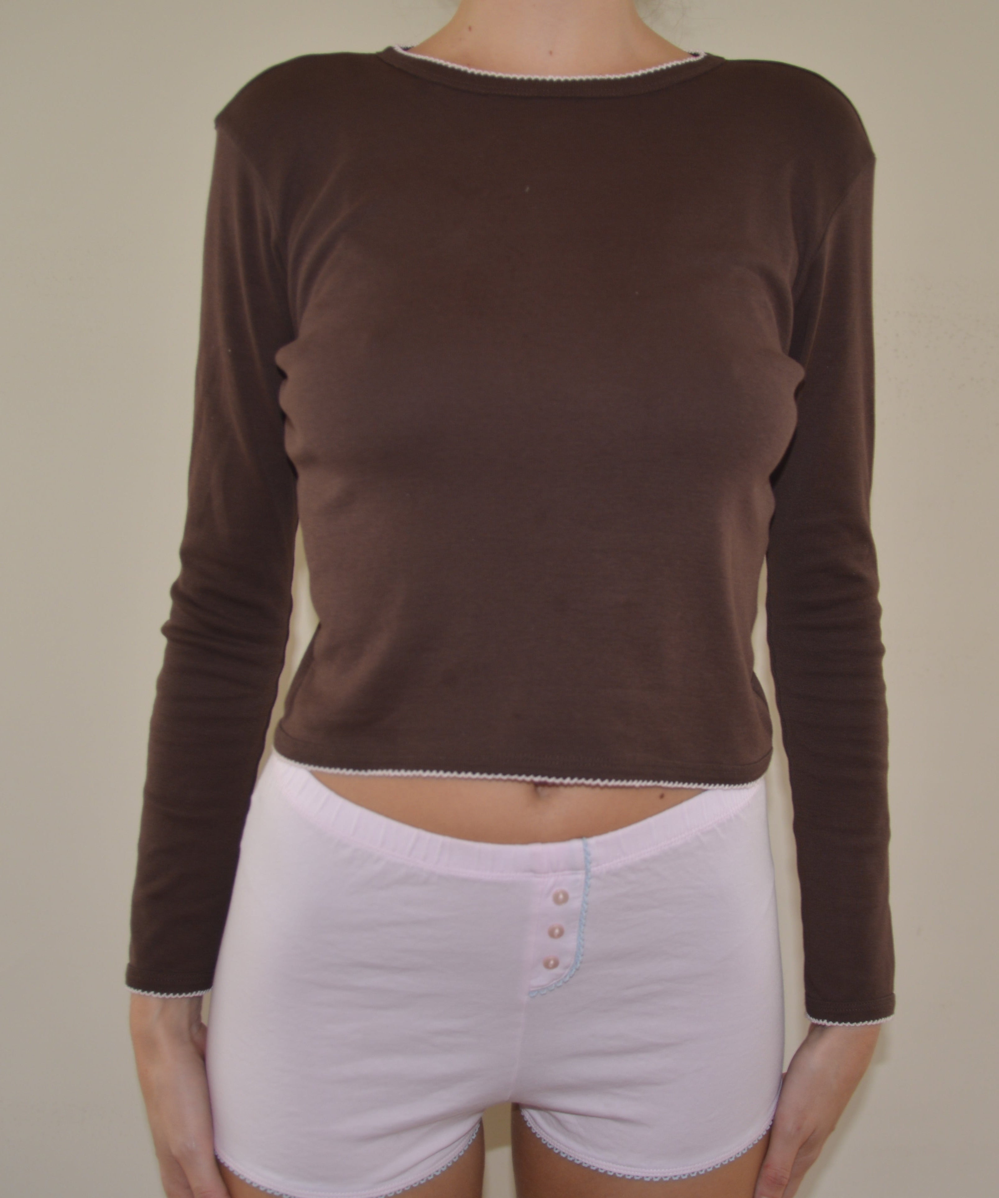 Person wearing a brown long-sleeve top and pink shorts on a plain background